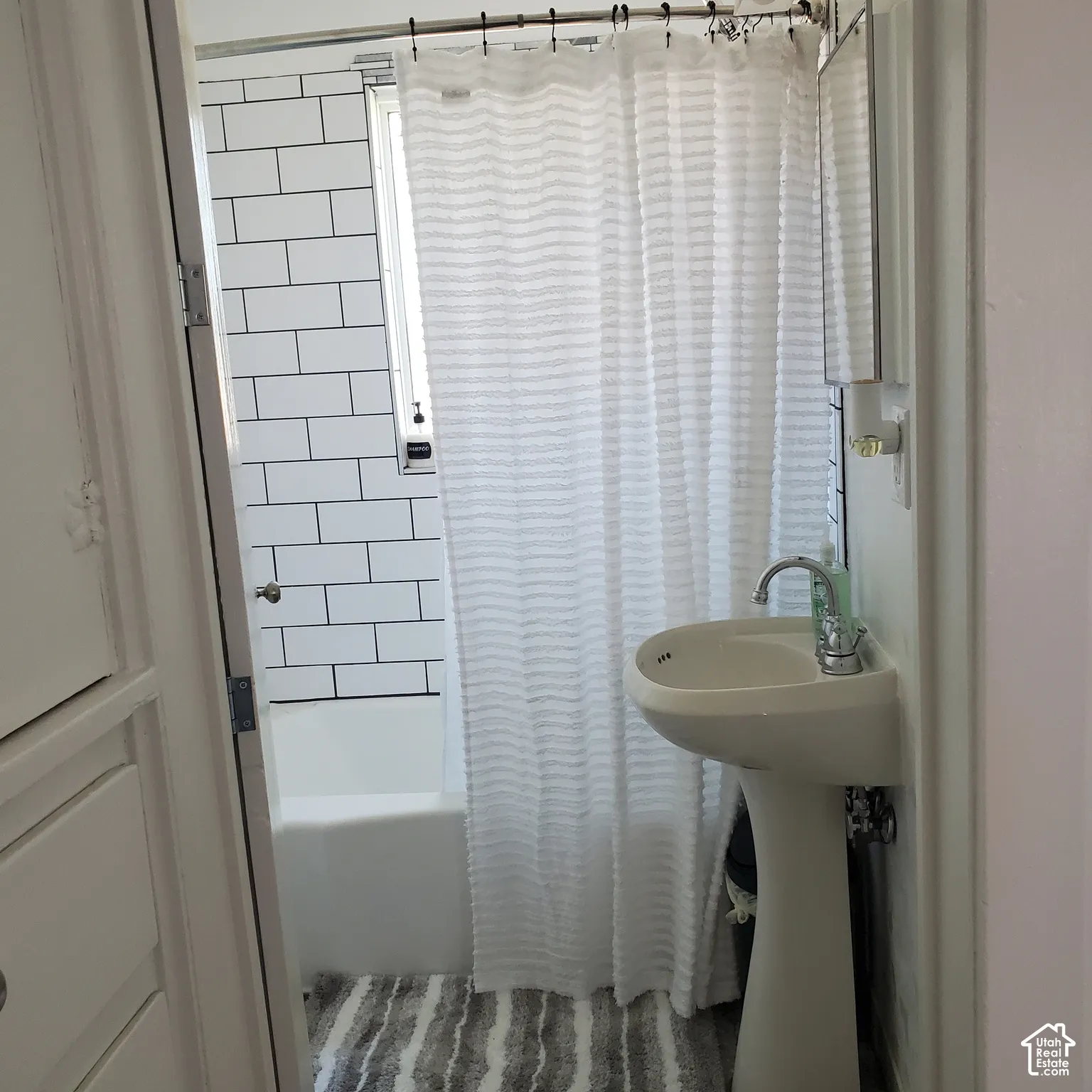 Bathroom featuring a white pedestal sink, chrome faucet, bathtub surround with white subway tile and dark grout.