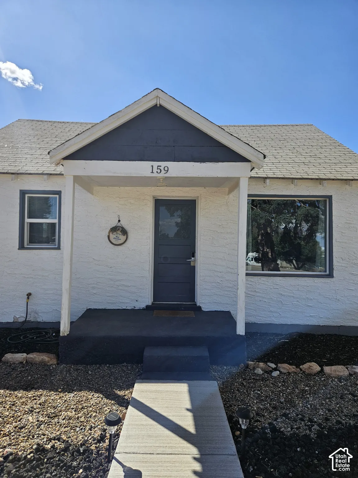 Textured white exterior with a covered front porch, dark-painted trim, concrete entryway, and rock-based landscaping