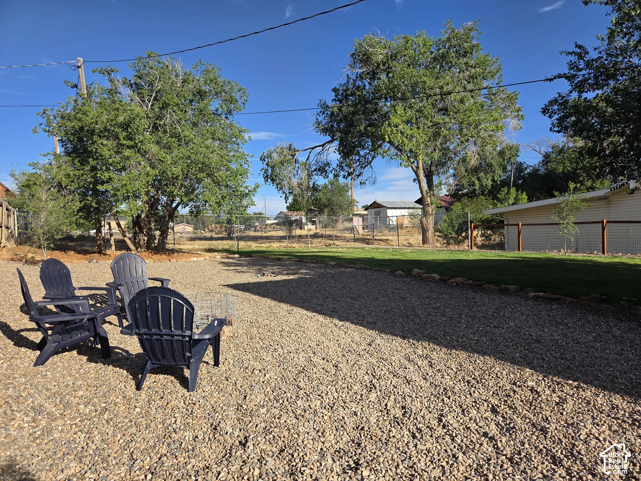Private - expansive outdoor space featuring a graveled ground cover, manicured lawn area, mature trees, and perimeter fencing.