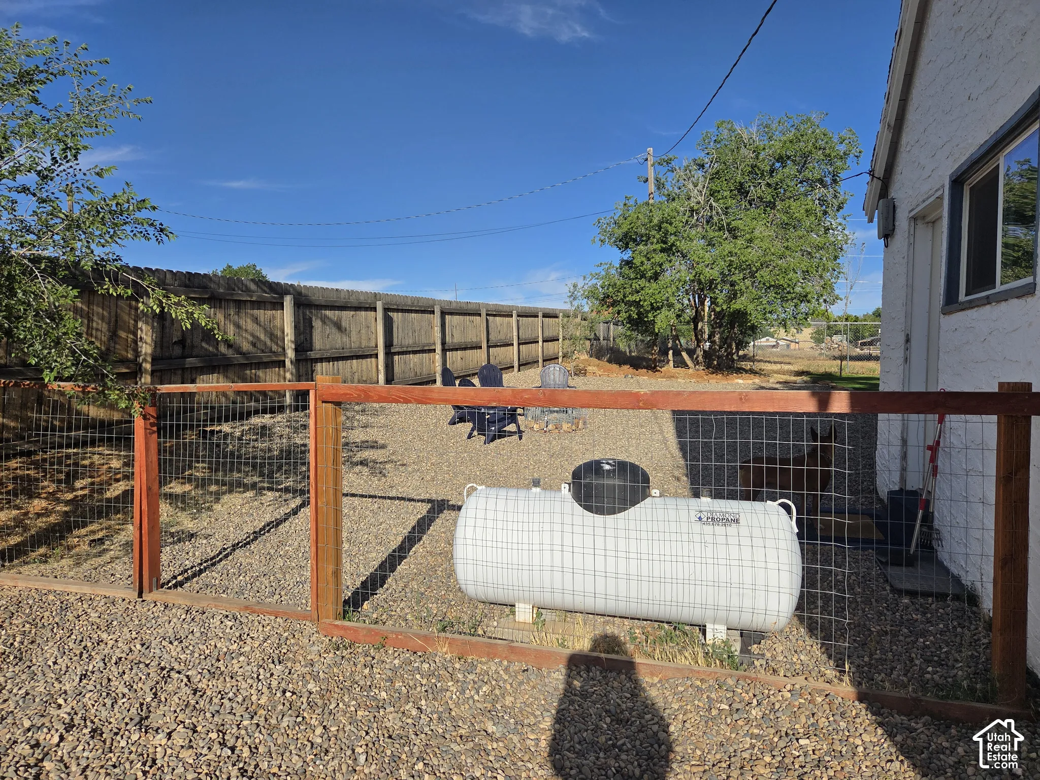 Exterior space featuring a gravel-surfaced yard, wood-frame wire fencing, and an on-site propane tank (Propane tank is rented and runs the fire pit on a timer)