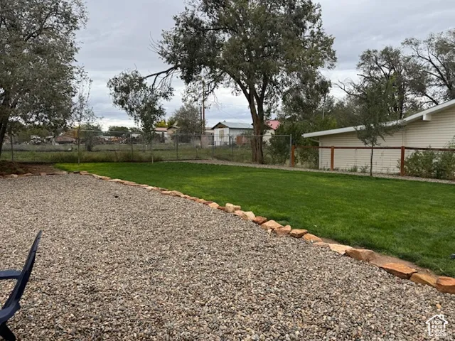 Backyard featuring a leveled lawn, gravel hardscaping, natural stone edging, perimeter fencing, and mature trees.