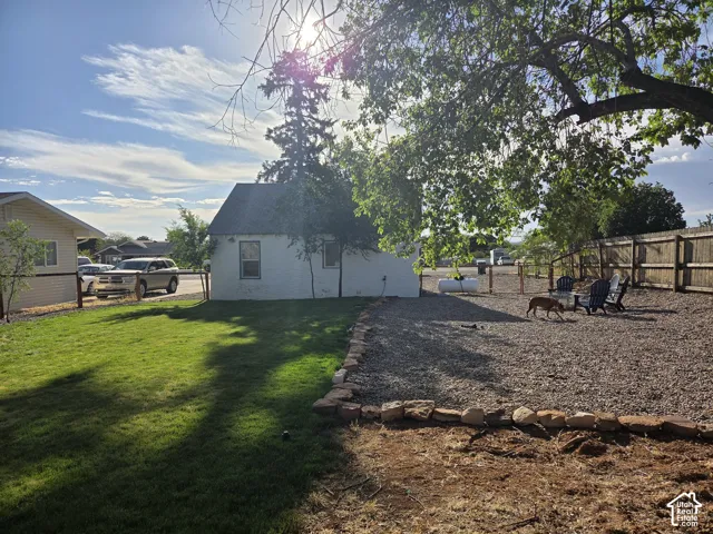 Backyard featuring a combination of lawn and gravel ground cover, split-rail style fencing, natural stone bordering, and a mature tree.