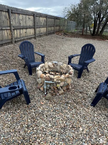 Outdoor space featuring a gabion-style stone fire pit with gas plumbing with built in timer, finished with decorative gravel ground cover and a wood-slat perimeter fence.