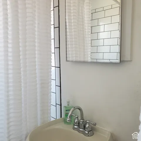 Wall-mounted medicine cabinet with a mirrored door, pedestal sink, chrome widespread faucet, and shower surround featuring white subway tile with black grout