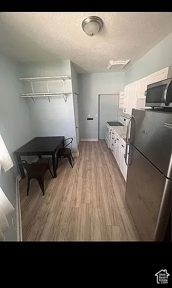 Kitchen featuring stainless steel appliances, wood-finish flooring, white cabinetry, a stone-composite countertop, and wall-mounted shelving