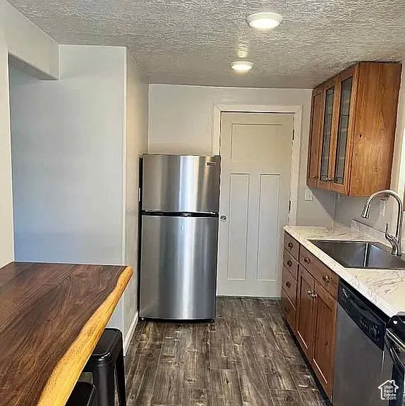 Kitchen featuring wood cabinetry with glass-panel inserts, live-edge wood breakfast bar, stainless steel appliances, stone-surface countertops, and wood-finish flooring