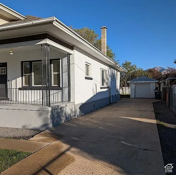 Painted brick exterior featuring a covered front porch with metal railings, a concrete driveway, and a detached garage