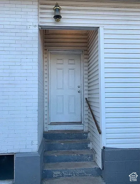 Exterior entryway featuring white horizontal siding, painted brick facade, concrete steps, and a wall-mounted light fixture
