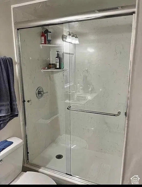 Walk-in shower enclosure featuring floor-to-ceiling surround panels, a sliding glass door with chrome hardware, an integrated corner shelving unit, and a polished chrome fixture