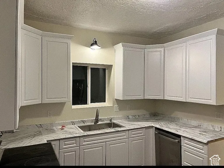 White shaker-style cabinetry, stone-patterned countertops with matching backsplash, stainless steel under-mount sink, integrated faucet, and built-in stainless steel dishwasher