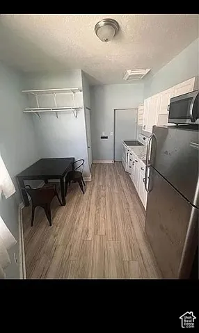 Kitchen featuring stainless steel appliances, wood-finish flooring, white cabinetry, a stone-composite countertop, and wall-mounted shelving
