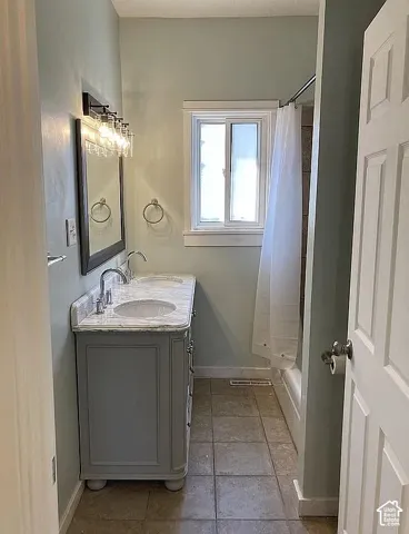Bathroom featuring a double vanity with stone-top surface, undermount sinks, tile flooring, and a shower-tub combination