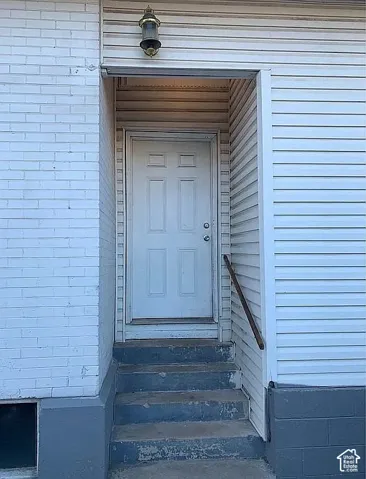 Exterior entryway featuring white horizontal siding, painted brick facade, concrete steps, and a wall-mounted light fixture