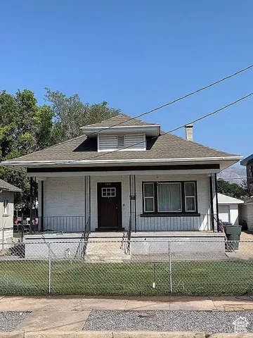 Single-story exterior featuring a brick facade, covered front porch, hipped roofline, dormer window, and paneled front door