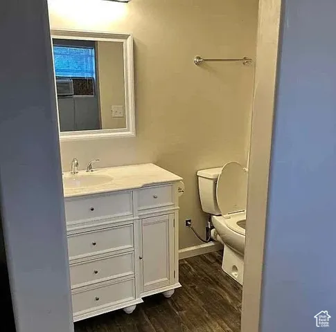 White vanity featuring a stone-surface countertop, integrated basin, brushed metal hardware, and wood-finish flooring