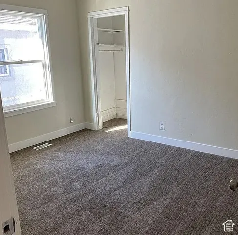 Neutral wall tones, wall-to-wall carpeting, window with paneled trim, and reach-in closet featuring built-in shelving
