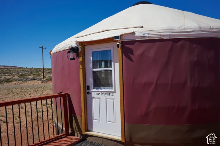 Circular yurt exterior featuring a tensioned fabric shell, white framed entry door with inset glass, metal railing, and wall-mounted exterior lighting