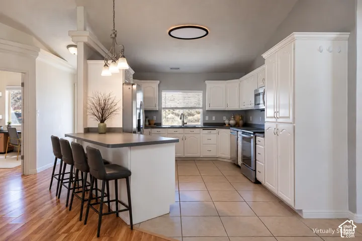 Kitchen featuring white cabinetry, solid surface countertops, stainless steel appliances, a peninsula island with bar seating, and tile flooring