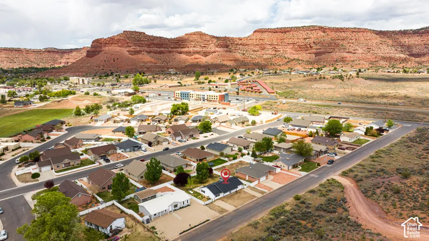 Aerial perspective of a single-story residence featuring a concrete driveway, paved street access, desert landscape, and red rock mountain backdrop