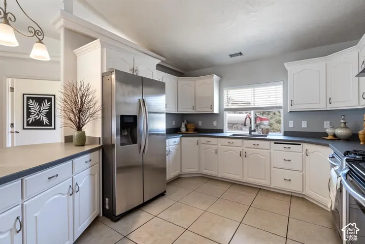 Kitchen featuring white cabinetry, solid-surface countertops, tile flooring, stainless steel side-by-side refrigerator, and a dual-basin undermount sink