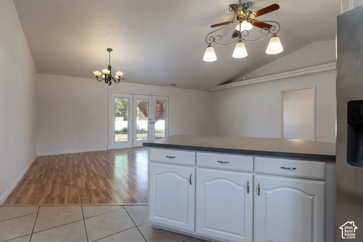 Vaulted ceilings, white cabinetry with stone-finish countertops, wood-finish flooring, dual-light chandeliers, and French doors