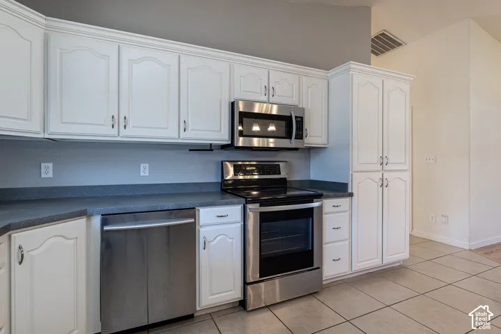 Kitchen featuring white cabinetry, stainless steel appliances, dark countertops, and tile flooring