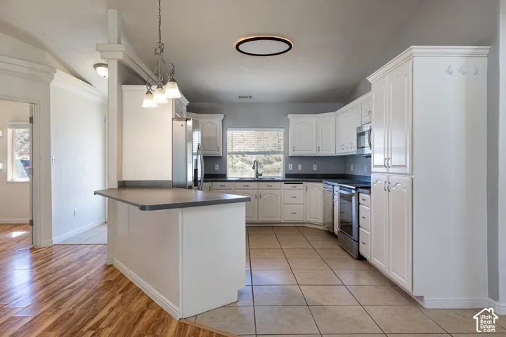 Kitchen featuring white cabinetry, solid-surface countertops, tile flooring, stainless steel appliances, and a three-light pendant fixture