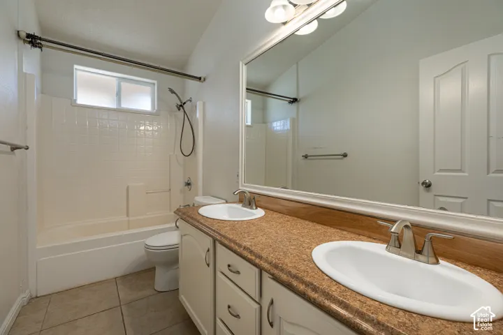 Bathroom featuring a dual-sink vanity with speckled stone-finish countertops, full-width mirror, tile flooring, and a combined tub and shower enclosure