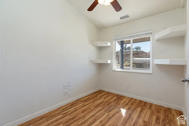Room featuring wood-finish flooring, built-in corner shelving, a ceiling fan, and a window with blinds