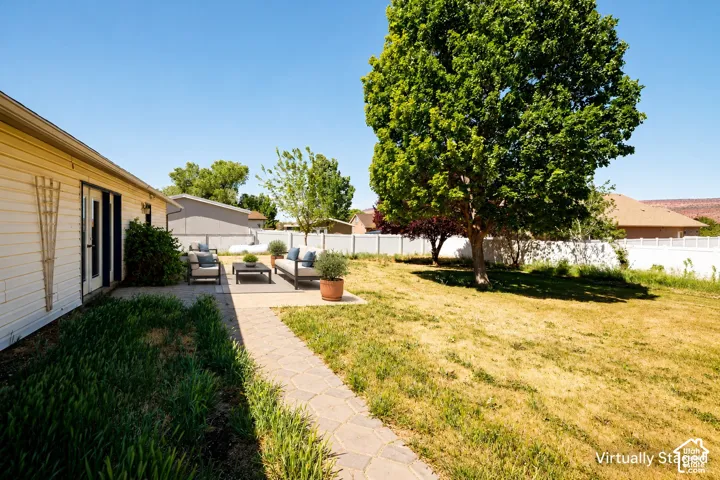 Spacious backyard featuring a concrete paver patio, vinyl perimeter fencing, and a mature shade tree