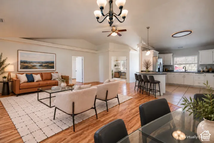 Vaulted ceilings, wood-finish flooring, kitchen island with breakfast bar seating, classic chandelier, and neutral wall tones