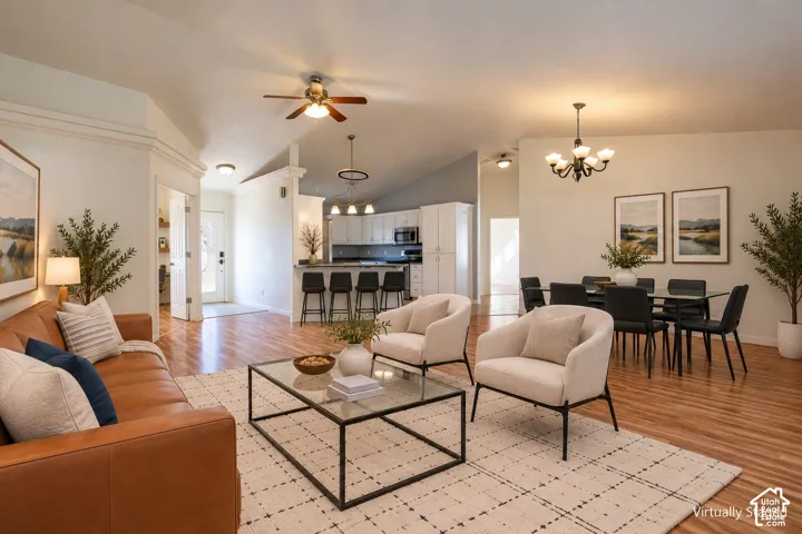 Open-concept interior featuring vaulted ceilings, wood-finish flooring, a kitchen breakfast bar, and multiple overhead light fixtures