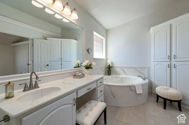 Bathroom featuring a vanity with integrated sink and countertop, full-width wall mirror, soaking tub with stone-finish surround, and floor-to-ceiling built-in cabinetry