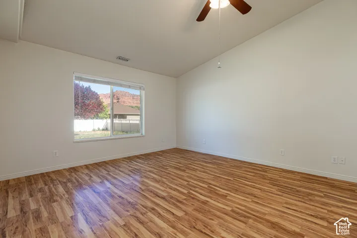 Vaulted ceilings, wood-finish flooring, ceiling fan with light fixture, and large window with red rock formation scenery