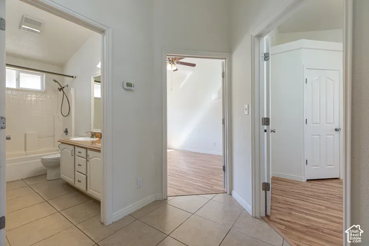 Bathroom featuring a vanity with wood-tone cabinetry and an integrated sink, tiled flooring, and a combined tub and shower unit, finished with wood-finish flooring in the surrounding spaces and interior doors with molded detailing