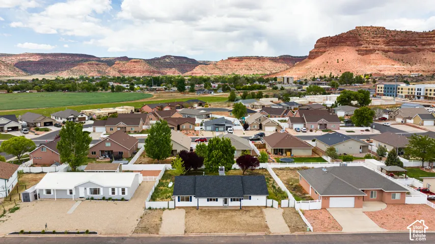 Aerial perspective of residential property featuring a white exterior, dark shingled roof, attached garage, and white perimeter fencing