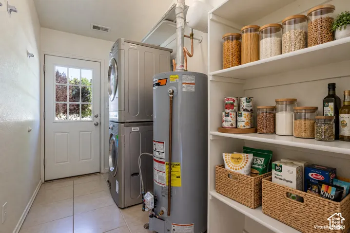 Utility room featuring tile flooring, built-in shelving, a glass-panel exterior door, and a stacked laundry unit