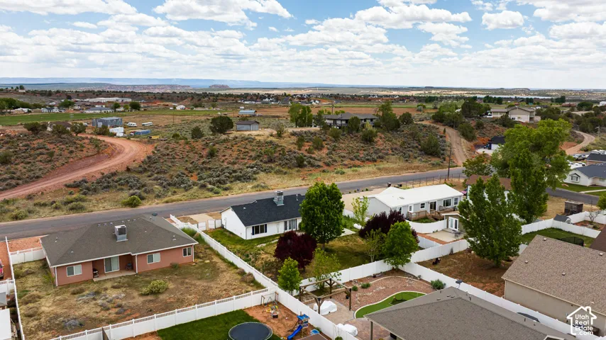 Aerial perspective of a residential neighborhood featuring white vinyl perimeter fencing, established mature trees, expansive desert terrain, and distant mesa landscapes