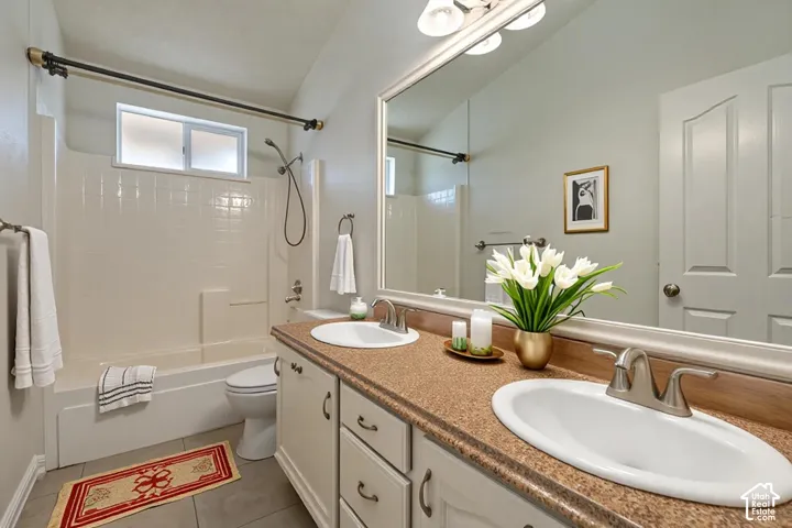 Bathroom featuring a double-sink vanity with a solid-surface countertop, full-width wall mirror, tub-and-shower combination, and tiled flooring