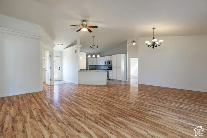 Open-concept floor plan featuring vaulted ceilings, wood-finish flooring, white cabinetry, a multi-light chandelier, and integrated ceiling fans