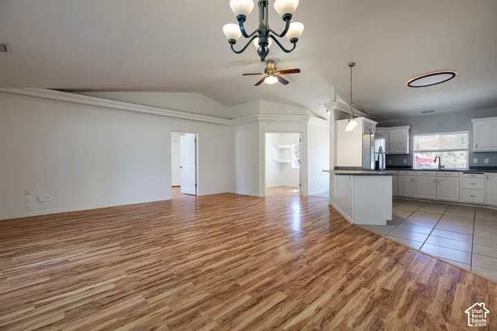 Vaulted ceilings, wood-finish flooring, kitchen featuring white cabinetry and a breakfast bar, and integrated multi-light chandelier and ceiling fan fixtures