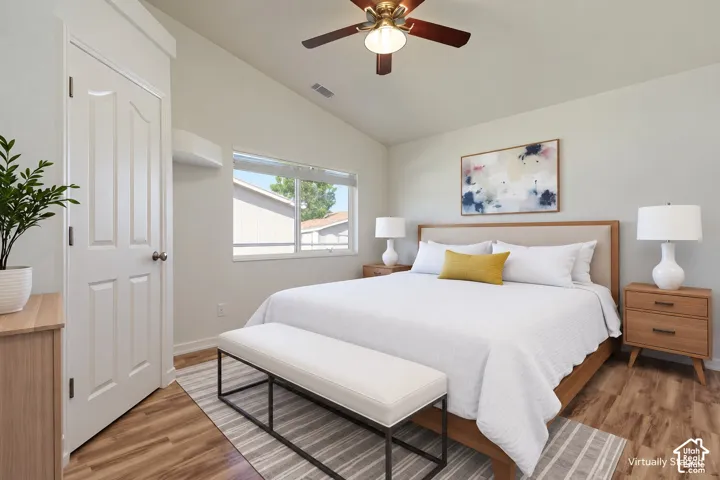Vaulted ceilings featuring a central overhead fan, wood-finish flooring, and a single-panel interior door