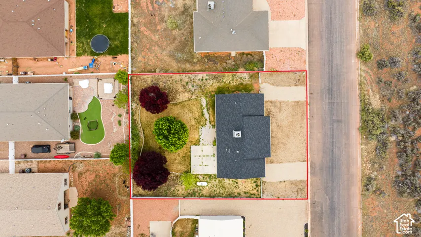 Aerial perspective of residential lot featuring a rectangular property boundary, shingle-roof structure, concrete patio, mature landscaping, and an expansive side-yard area