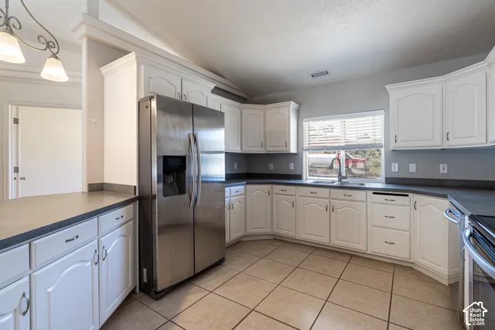 Kitchen featuring white raised-panel cabinetry, dark solid-surface countertops, stainless steel side-by-side refrigerator, tile flooring, and a stainless steel dual-basin sink with a gooseneck faucet