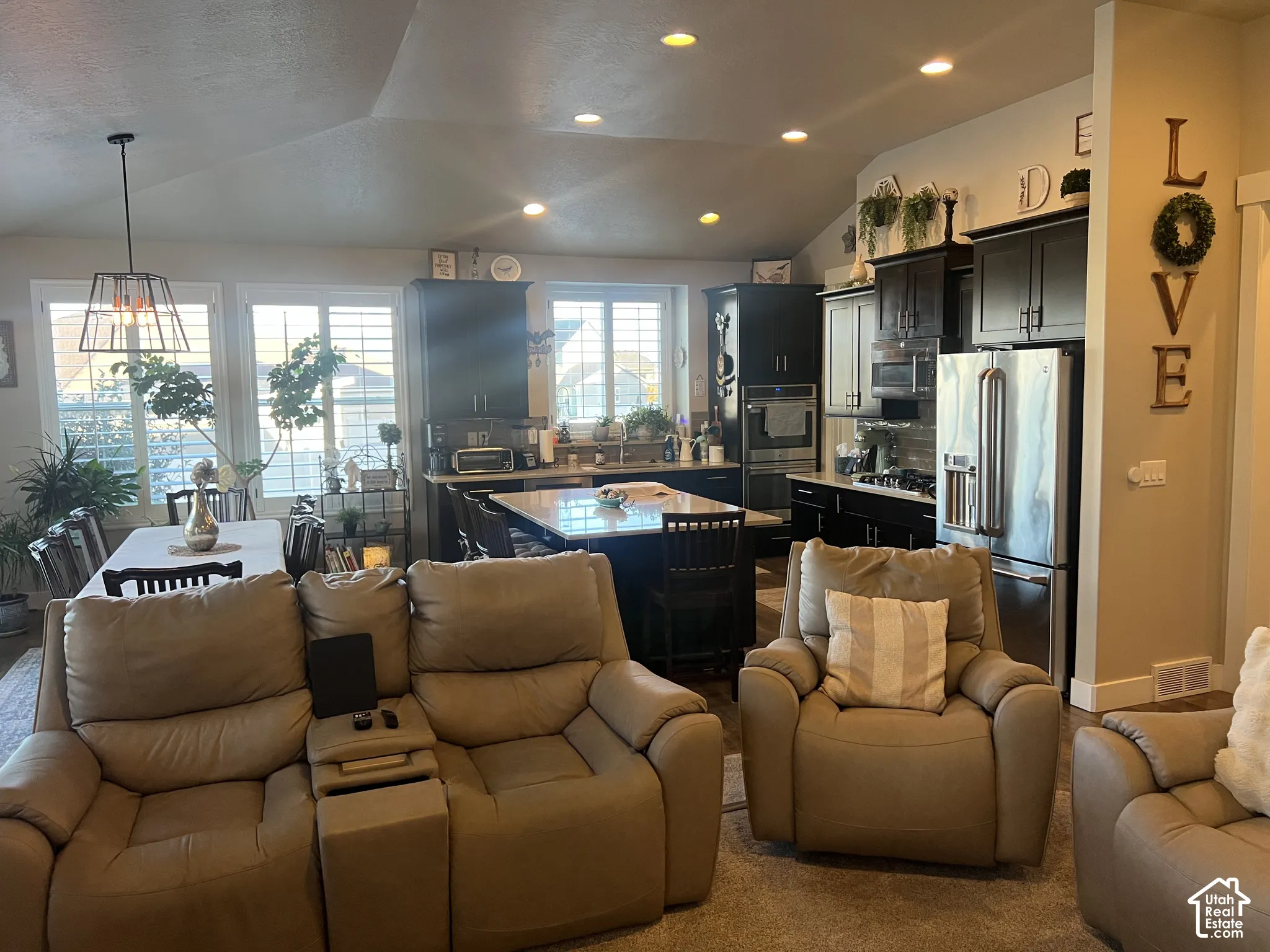 Kitchen featuring dark cabinetry, a central island with a stone countertop, stainless steel appliances, recessed ceiling lighting, and large windows with interior shutters