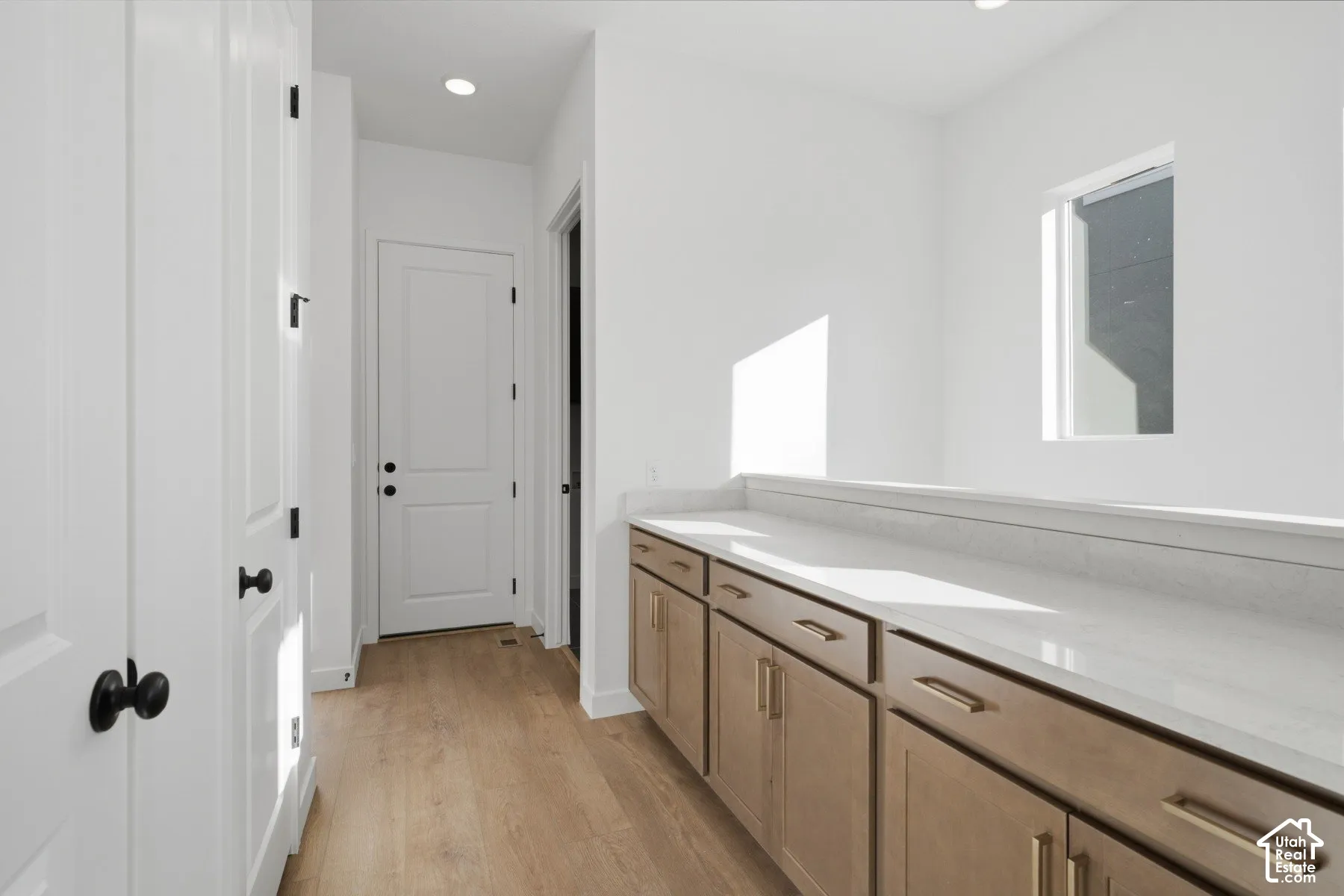 Natural-finish cabinetry with metallic hardware, stone-surface countertop, wood-finish flooring, recessed lighting, and multi-panel interior doors with matte black hardware
