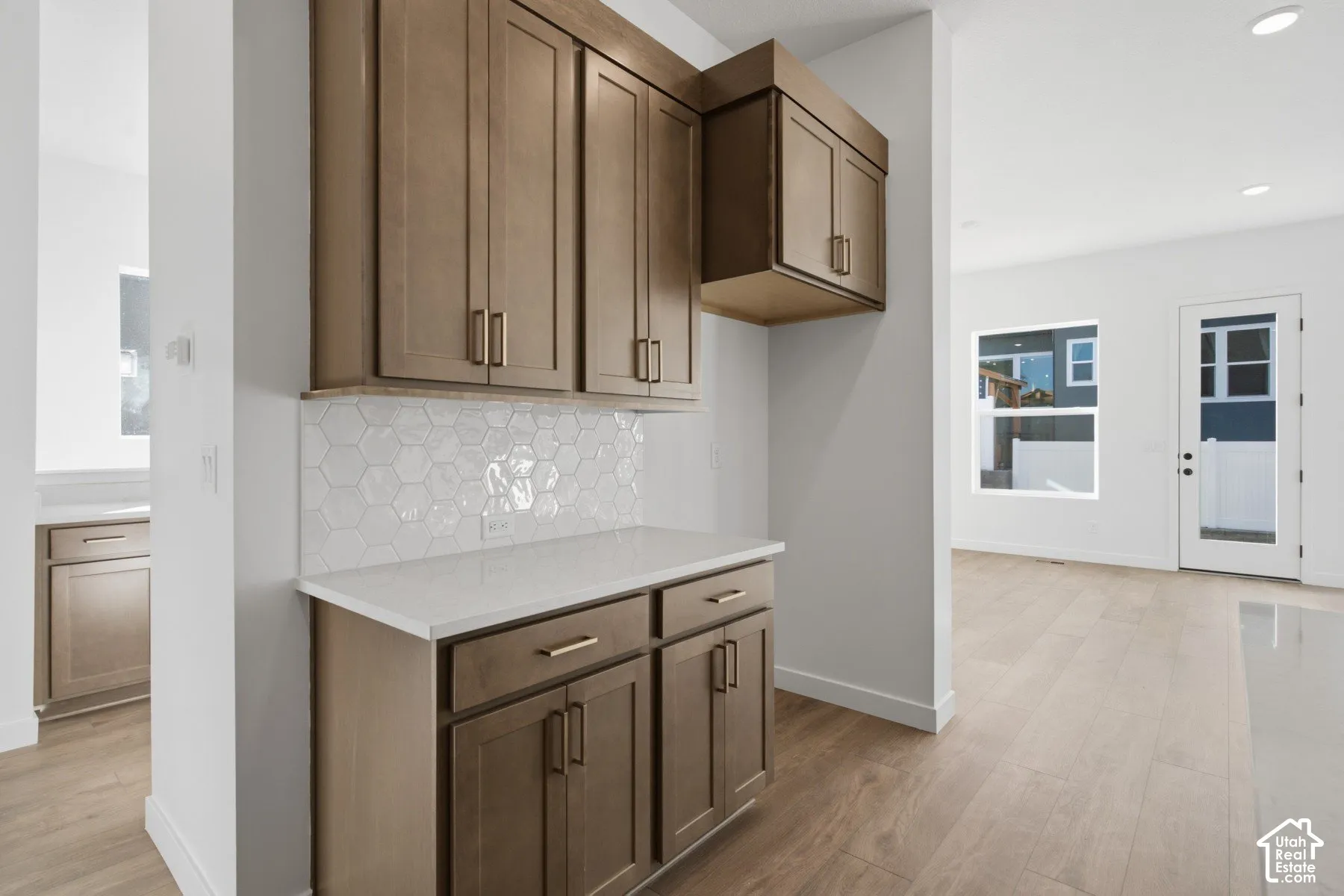 Custom cabinetry featuring shaker-style doors, matte finish hardware, quartz countertops, white hexagonal tile backsplash, and wood-finish flooring