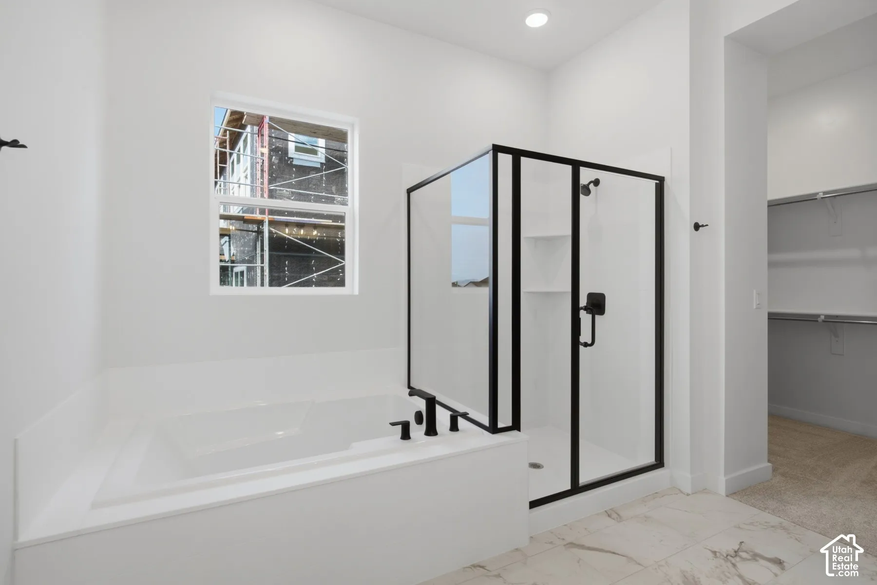 Built-in soaking tub with deck, glass-enclosed shower with matte black fixtures, and walk-in closet with integrated shelving