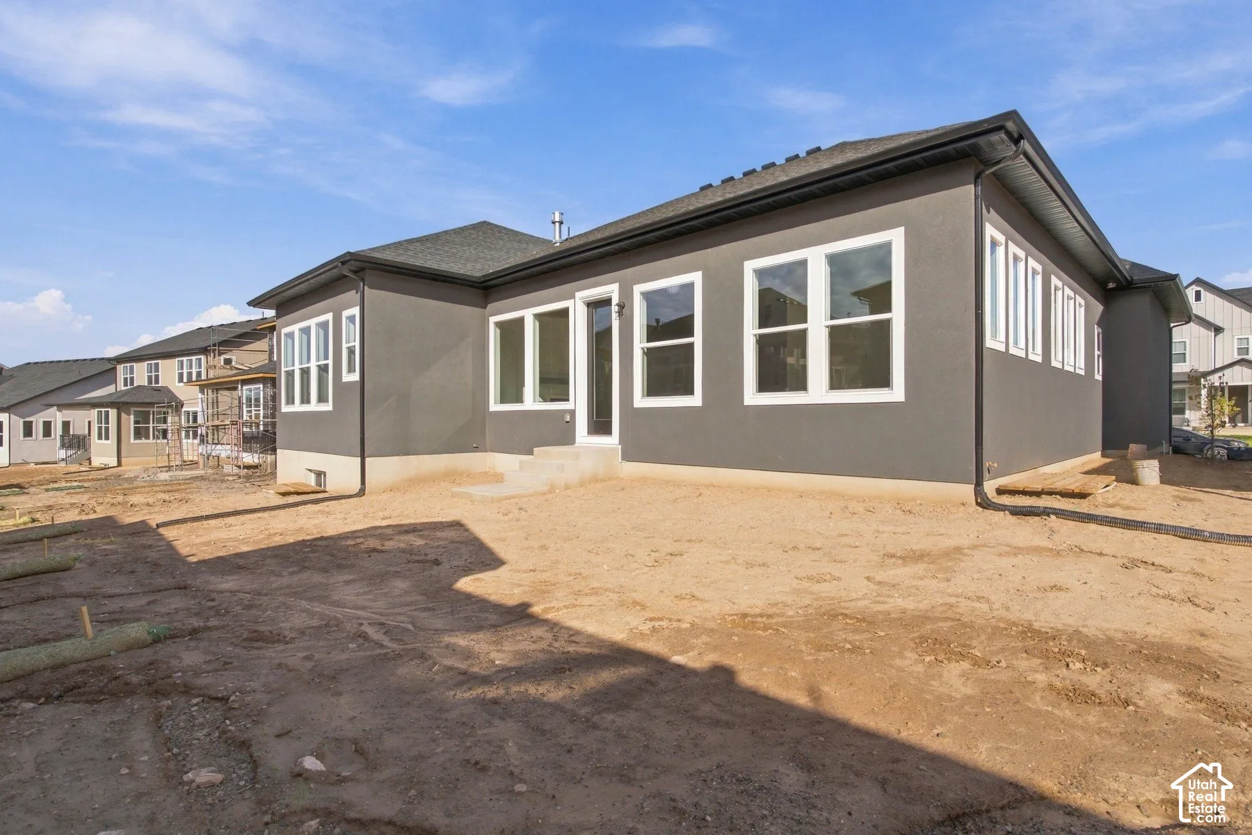 Rear exterior featuring smooth dark-toned stucco siding, dark-toned asphalt shingle roofing, expansive multi-pane windows, and a concrete entry pad
