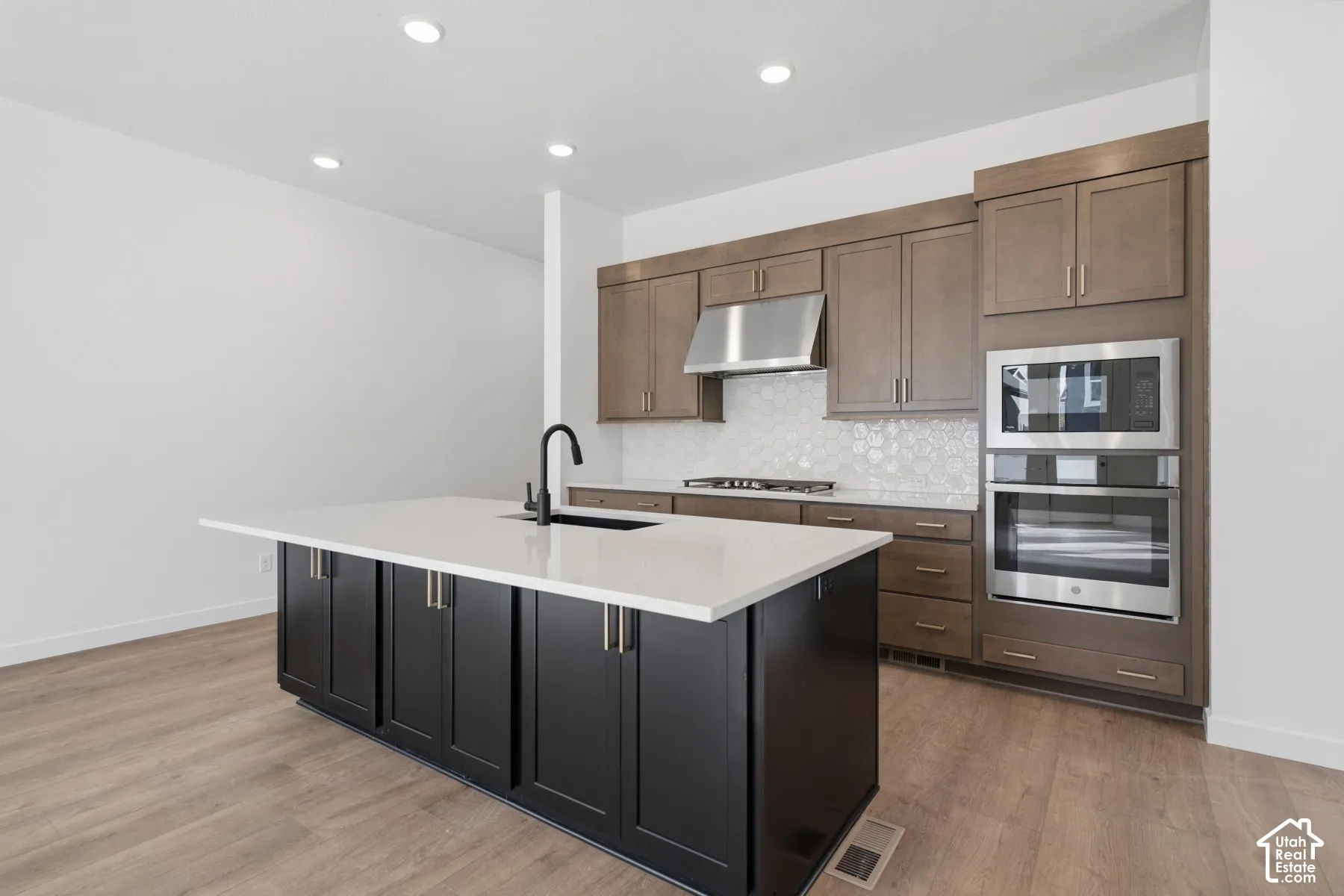 Kitchen featuring a center island with quartz countertops, custom cabinetry, stainless steel double wall ovens, a gas cooktop with a stainless steel range hood, and wood-finish flooring
